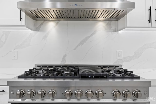 kitchen view of wall chimney range hood, backsplash, and white cabinetry