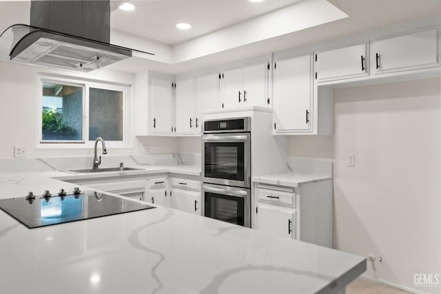 kitchen with a sink, island range hood, double oven, black electric stovetop, and light stone countertops
