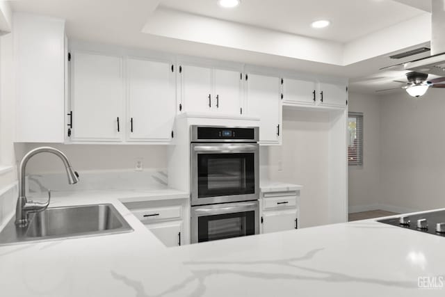 kitchen featuring stainless steel double oven, a tray ceiling, a sink, and recessed lighting