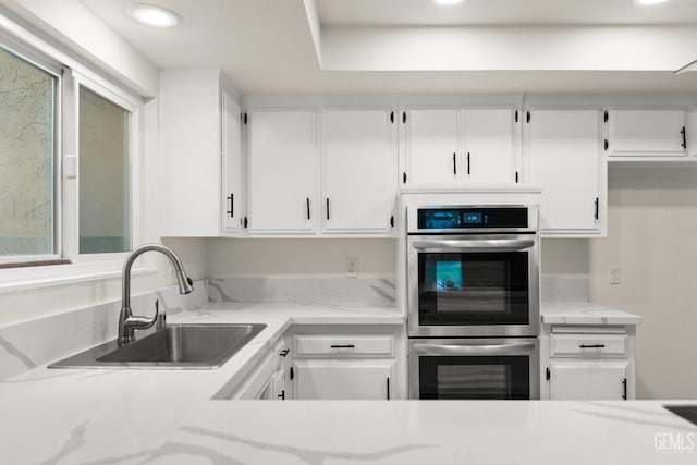 kitchen featuring recessed lighting, stainless steel double oven, light stone counters, a sink, and white cabinetry