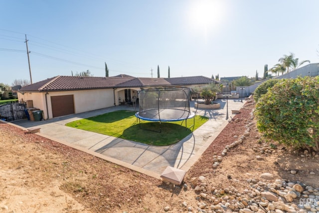 single story home with a tiled roof, an attached garage, a trampoline, a front lawn, and stucco siding