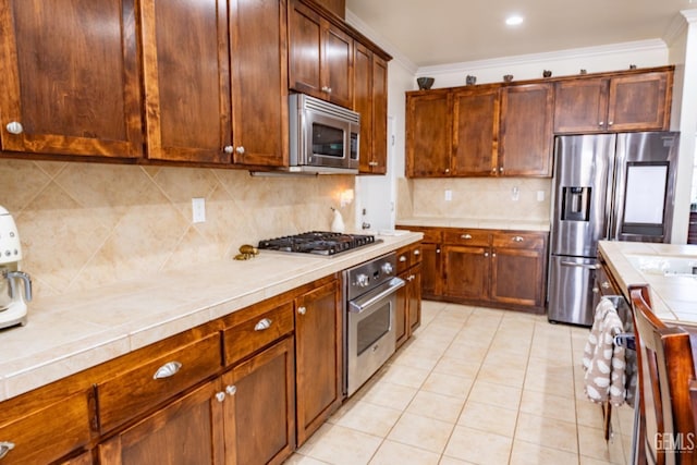 kitchen featuring tile countertops, appliances with stainless steel finishes, light tile patterned floors, and crown molding