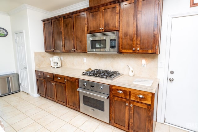 kitchen featuring light tile patterned floors, ornamental molding, appliances with stainless steel finishes, tile counters, and tasteful backsplash