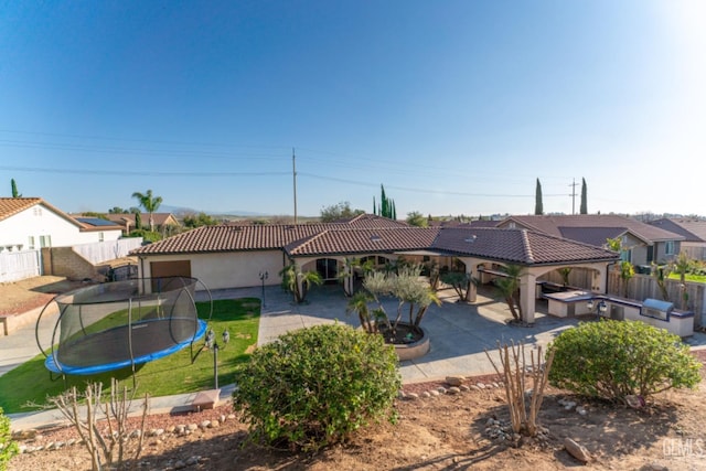 view of front of home featuring fence, a tiled roof, exterior kitchen, a trampoline, and a patio area