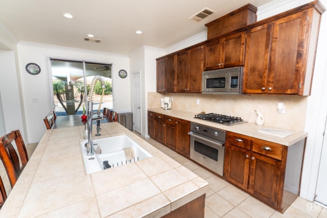 kitchen with stainless steel appliances, a sink, visible vents, backsplash, and tile counters