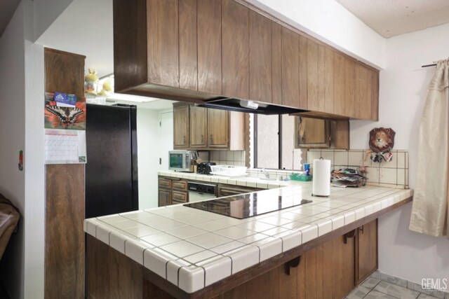 5116 Sherman Ave, Bakersfield, CA 93309 - kitchen featuring black electric stovetop, tile counters, light tile patterned floors, and kitchen peninsula