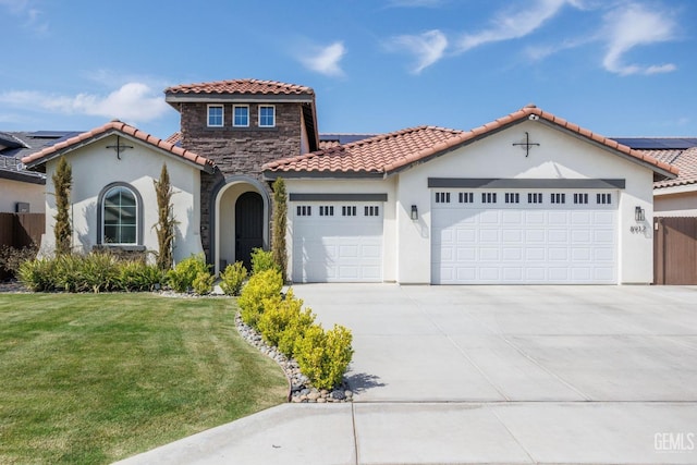 mediterranean / spanish home featuring stucco siding, concrete driveway, a garage, stone siding, and a front lawn