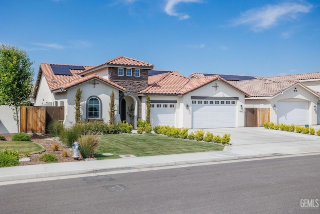 mediterranean / spanish-style house featuring an attached garage, fence, concrete driveway, roof mounted solar panels, and a front yard