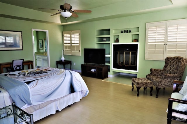 bedroom with ceiling fan, a tray ceiling, ensuite bathroom, and hardwood / wood-style flooring