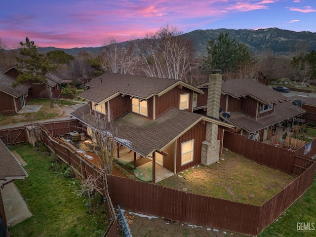 rear view of property featuring a lawn, a fenced backyard, a chimney, roof with shingles, and a mountain view