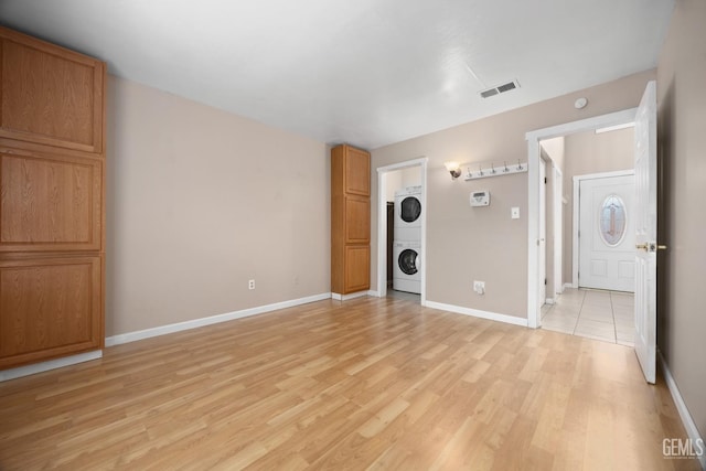 unfurnished room with light wood finished floors, stacked washing maching and dryer, visible vents, and baseboards