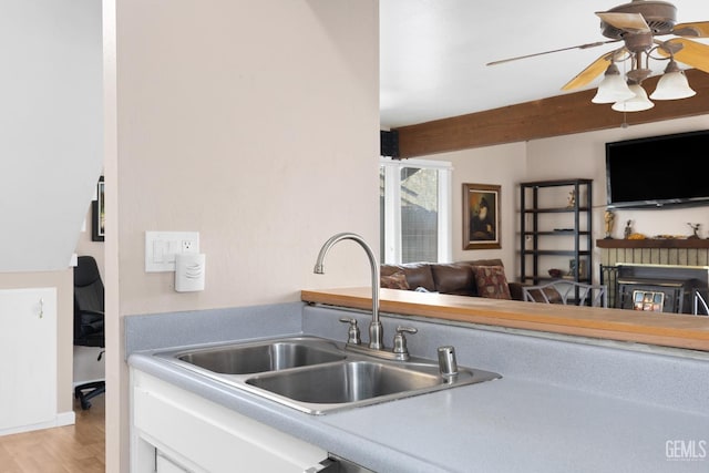 kitchen featuring light wood finished floors, light countertops, a glass covered fireplace, open floor plan, and a sink