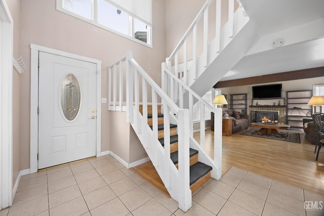 foyer with light tile patterned floors, a high ceiling, stairway, and a glass covered fireplace