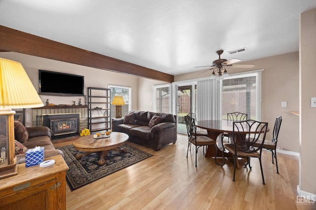 living area with light wood-type flooring, baseboards, visible vents, and a glass covered fireplace