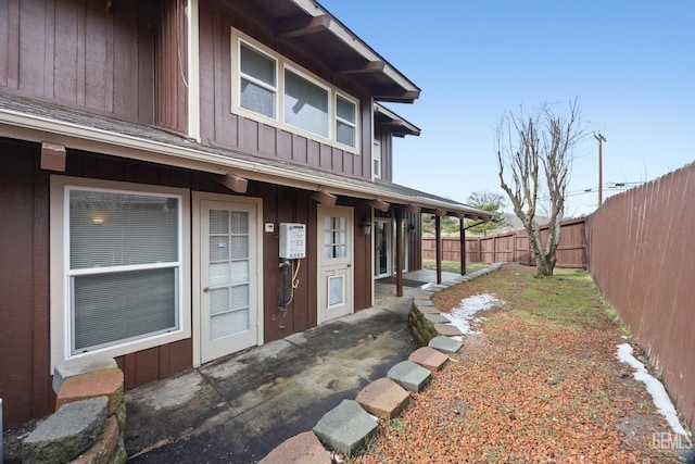 entrance to property featuring board and batten siding, fence, and a patio