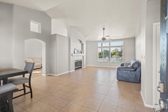 living area with ceiling fan, vaulted ceiling, light tile patterned floors, a fireplace, and arched walkways