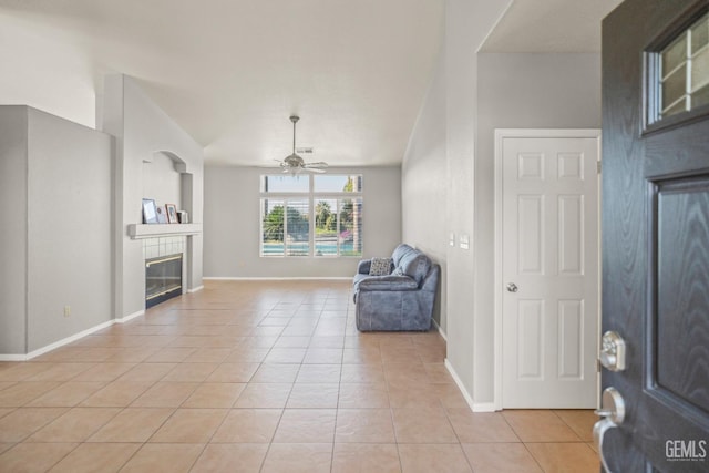 interior space with light tile patterned floors, baseboards, a ceiling fan, and a tile fireplace