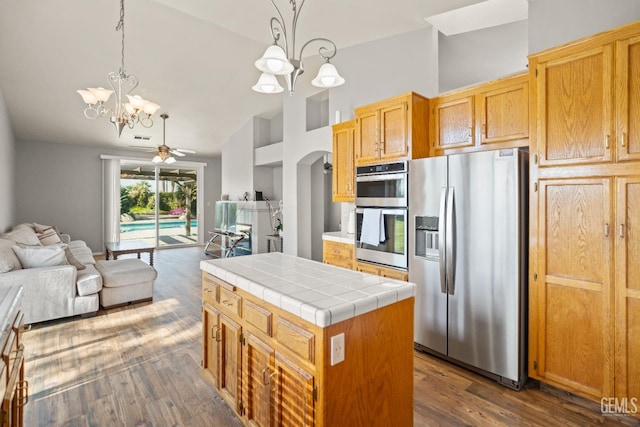 kitchen featuring open floor plan, a center island, stainless steel appliances, tile counters, and dark wood-style flooring