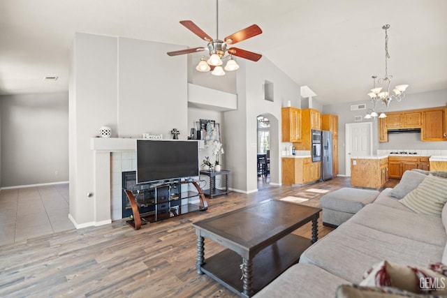 living area with visible vents, baseboards, ceiling fan with notable chandelier, wood finished floors, and high vaulted ceiling