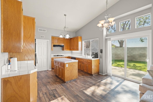 kitchen with visible vents, white gas cooktop, tile countertops, brown cabinetry, and a notable chandelier