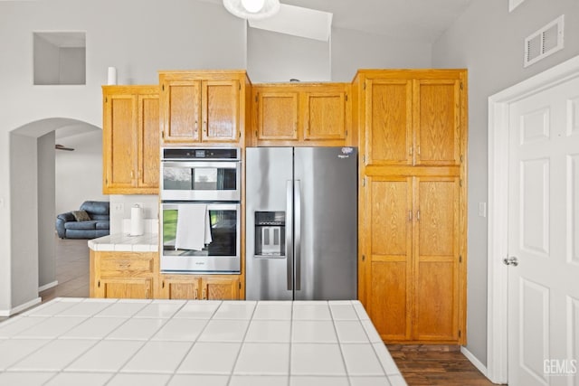 kitchen featuring visible vents, tile counters, vaulted ceiling, arched walkways, and stainless steel appliances