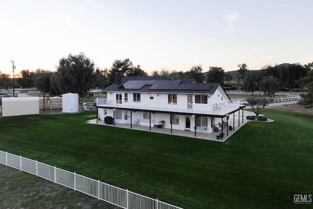 back of house at dusk featuring a lawn, solar panels, a fenced backyard, and a patio area