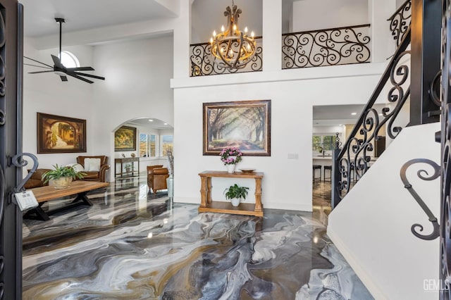 foyer featuring arched walkways, ceiling fan with notable chandelier, marble finish floor, stairs, and a towering ceiling