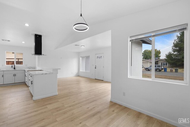 kitchen featuring sink, wall chimney exhaust hood, decorative light fixtures, white cabinets, and light wood-type flooring