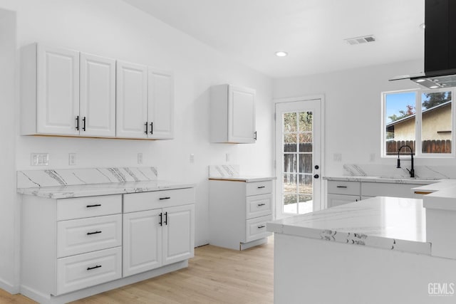 kitchen with light wood-type flooring, light stone counters, extractor fan, sink, and white cabinetry