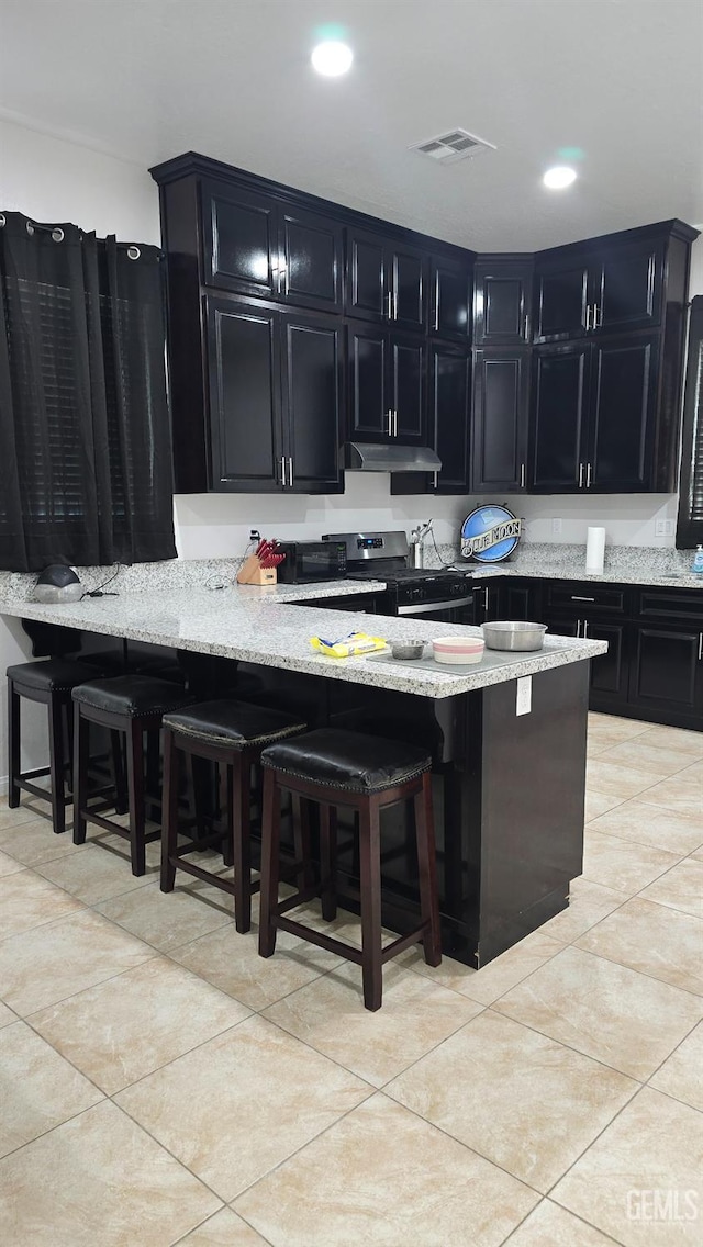 6304 Stanley St, Bakersfield, CA 93308 - kitchen featuring a kitchen breakfast bar, visible vents, stainless steel range with gas cooktop, light stone counters, and dark cabinetry