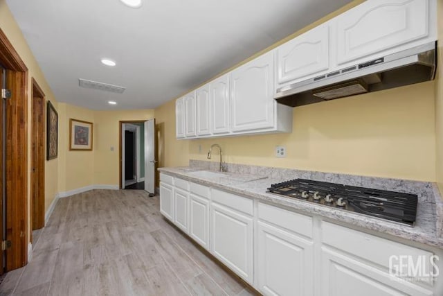 kitchen with light stone countertops, a sink, white cabinets, stainless steel gas stovetop, and under cabinet range hood
