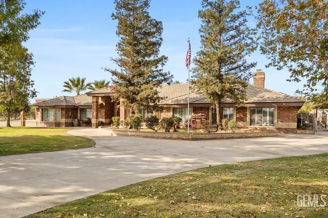 ranch-style home with concrete driveway, brick siding, a chimney, and a front yard