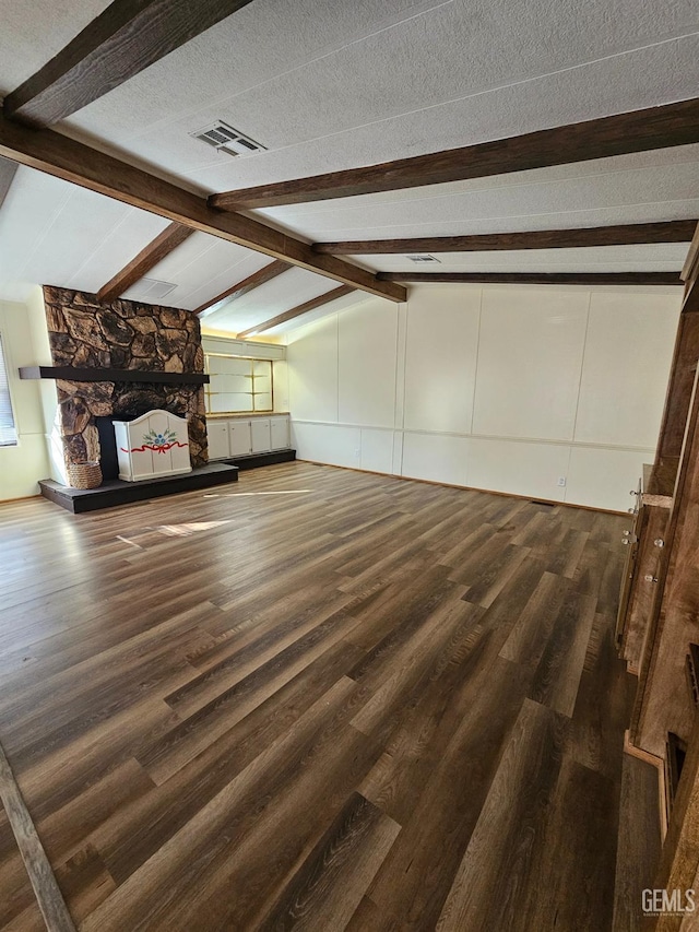 unfurnished living room with a textured ceiling, vaulted ceiling with beams, a stone fireplace, and dark wood-type flooring