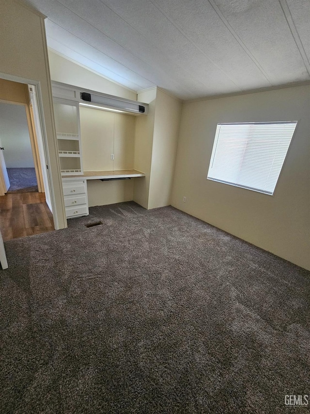 unfurnished bedroom featuring dark colored carpet, built in desk, a textured ceiling, and vaulted ceiling