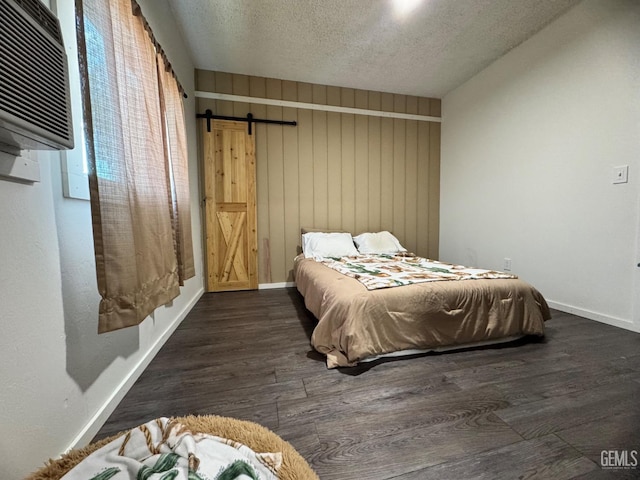 bedroom featuring baseboards, a barn door, a textured ceiling, wood finished floors, and a wall unit AC