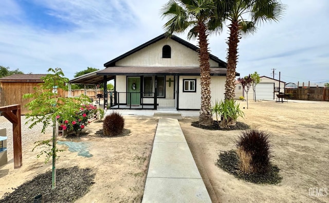 bungalow-style home with a porch, an outdoor structure, a garage, and fence