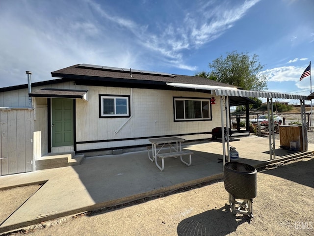 back of property with a patio area, solar panels, and a shingled roof