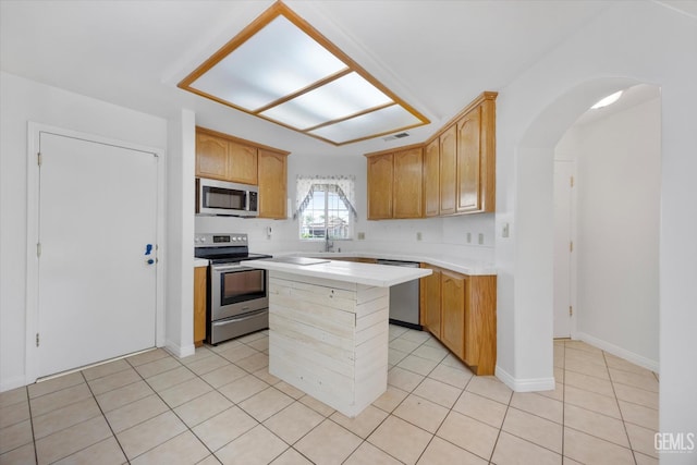 5820 Siena Ln, Bakersfield, CA 93308 - kitchen with appliances with stainless steel finishes, light countertops, light tile patterned floors, arched walkways, and a center island