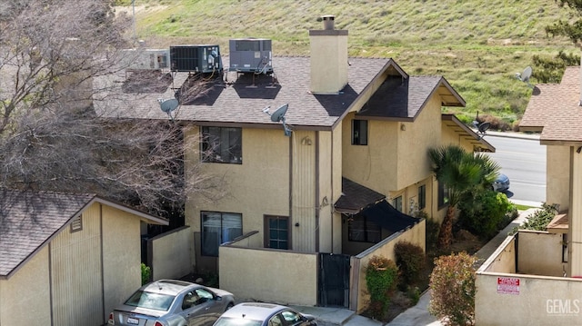 exterior space with central AC unit, a chimney, roof with shingles, and stucco siding