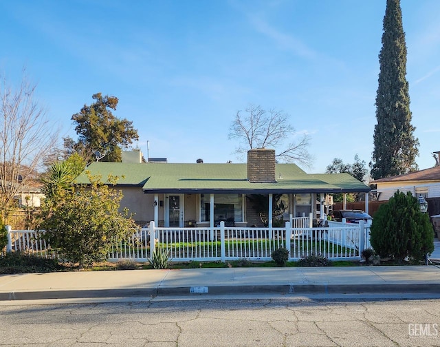 view of front facade featuring a fenced front yard, covered porch, a chimney, and stucco siding