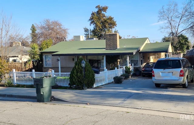 view of front of property with concrete driveway, covered porch, a fenced front yard, and a chimney