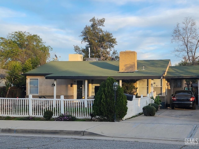 view of front facade featuring a fenced front yard, a carport, concrete driveway, and a chimney