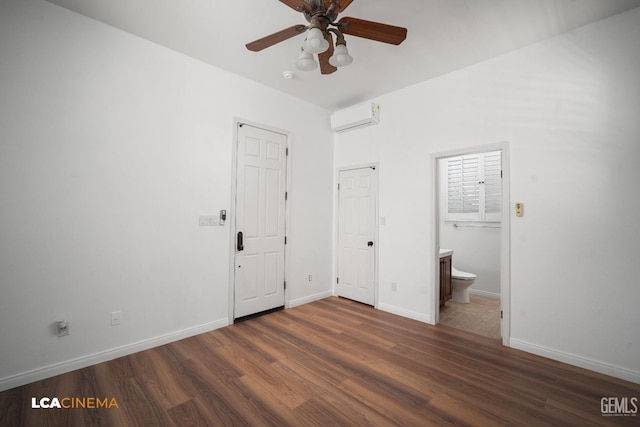 unfurnished bedroom with wood finished floors, a wall mounted AC, baseboards, ensuite bath, and a ceiling fan