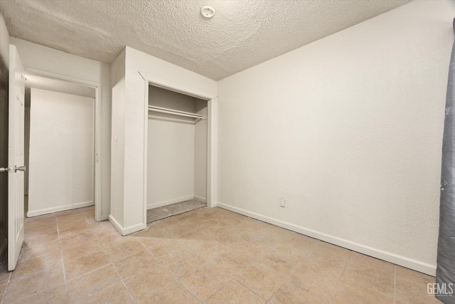 unfurnished bedroom featuring a closet, baseboards, light tile patterned floors, and a textured ceiling