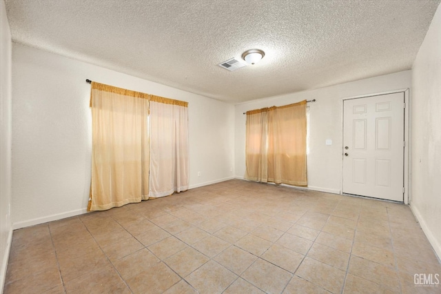 spare room with light tile patterned floors, visible vents, baseboards, and a textured ceiling