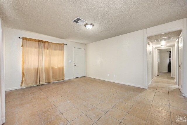 unfurnished room with a textured ceiling, light tile patterned floors, baseboards, and visible vents