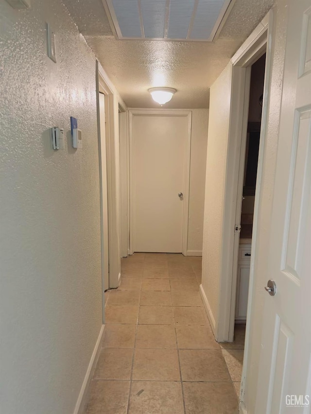 hallway with visible vents, a textured wall, a textured ceiling, and light tile patterned flooring