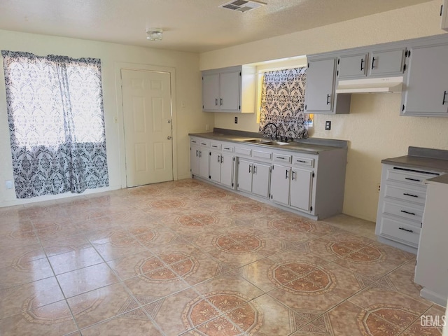 kitchen featuring light tile patterned flooring, dark countertops, under cabinet range hood, visible vents, and a sink