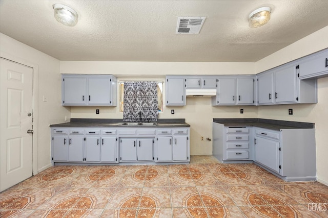 kitchen featuring a textured ceiling, visible vents, under cabinet range hood, dark countertops, and gray cabinetry