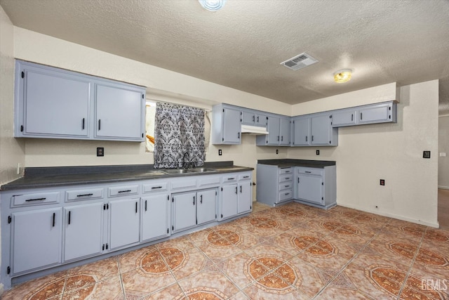 kitchen featuring a textured ceiling, blue cabinetry, visible vents, a sink, and dark countertops